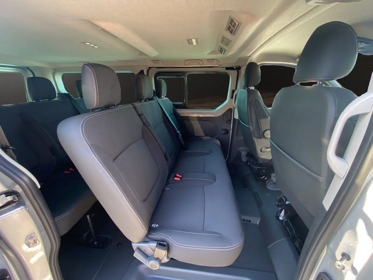 Vue intérieure côté droit du Renault Trafic Combi 2025, sièges tissu noir et porte coulissante ouverte.