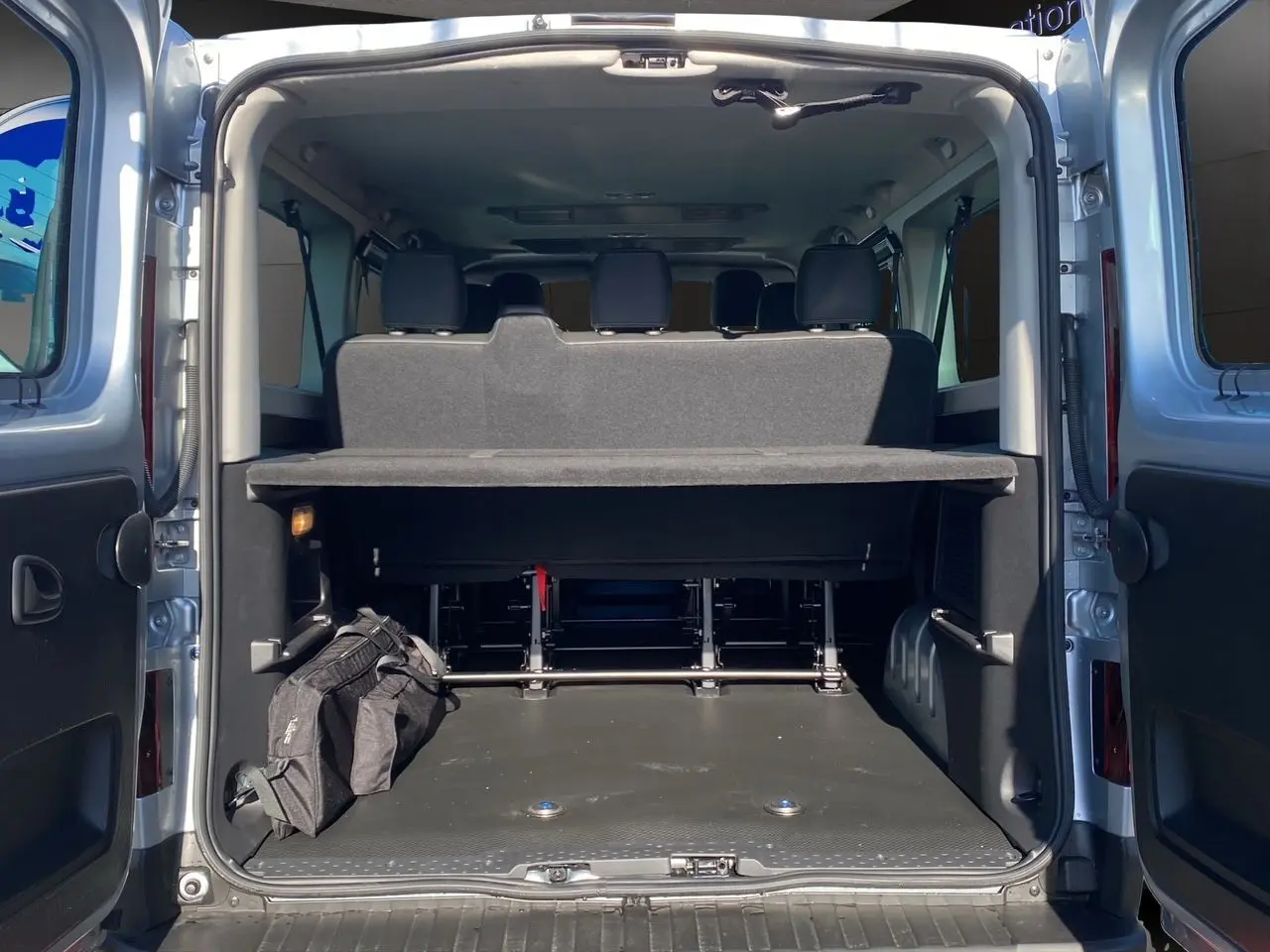 Vue arrière ouverte du Renault Trafic Combi gris Highland montrant le coffre spacieux avec banquette et sac noir.