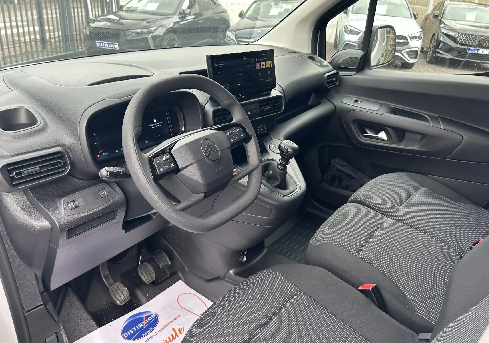 Intérieur du Citroën Berlingo Fourgon 2025 vu côté conducteur, avec tableau de bord noir et sièges tissu gris.