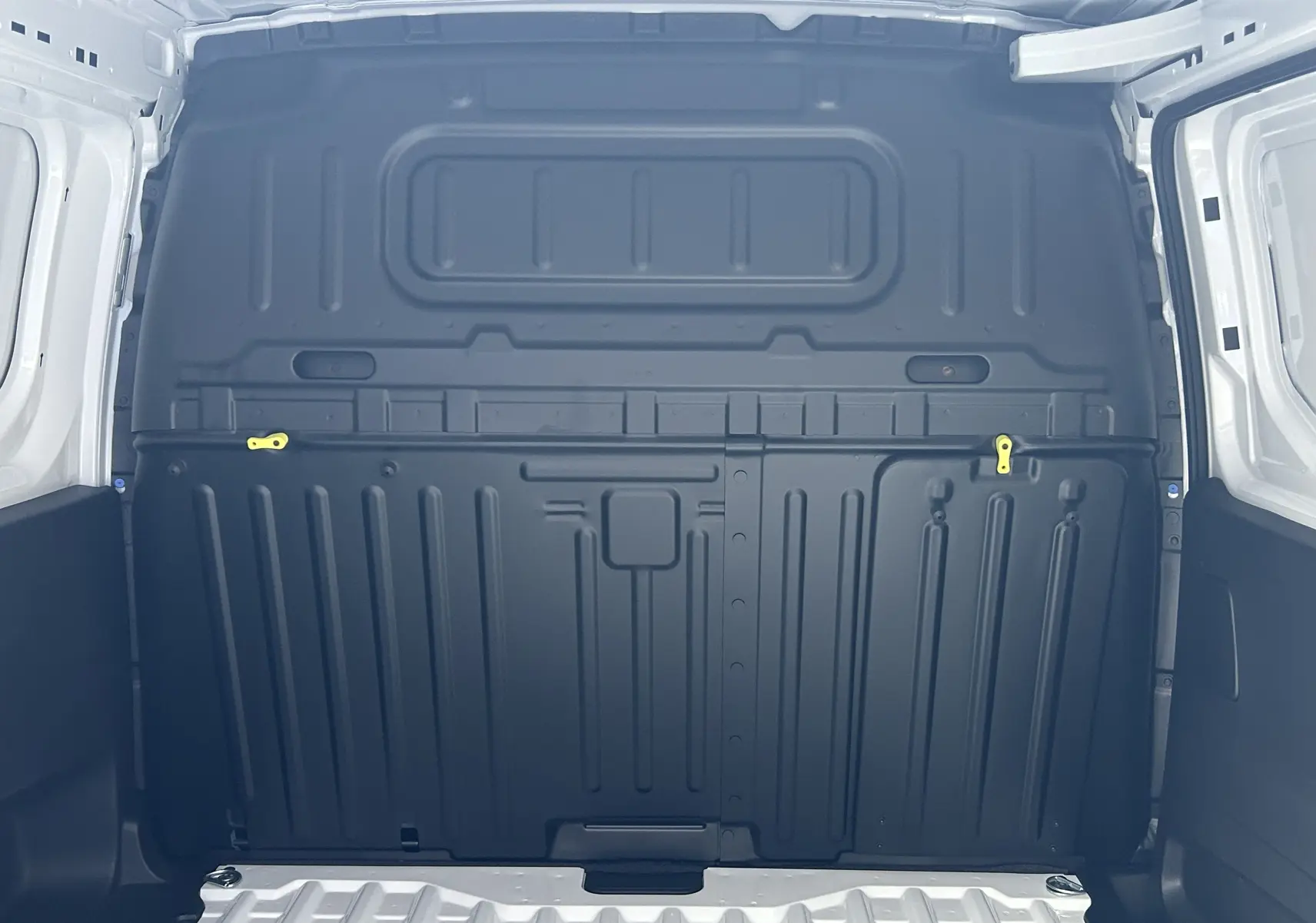 Intérieur du coffre du Citroën Berlingo Fourgon blanc 2025, montrant la cloison de séparation noire avec deux loquets jaunes.