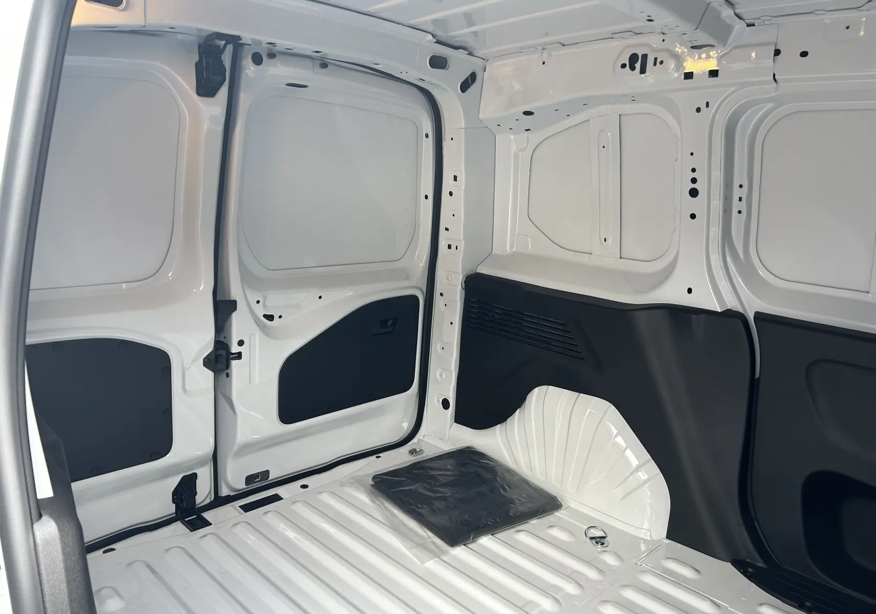 Intérieur du fourgon Citroën Berlingo BlueHDi 100 2025 en blanc, vue de la zone de chargement avec parois métalliques et protections noires.