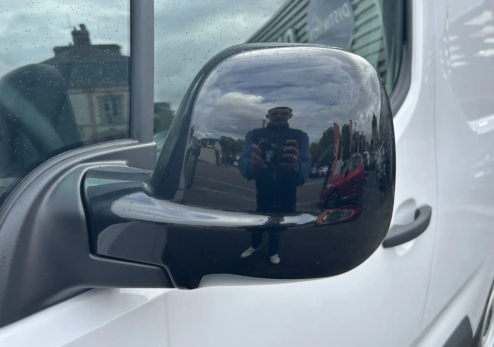 Rétroviseur noir côté gauche du Citroën Berlingo Fourgon blanc, avec reflet d'un photographe en extérieur.