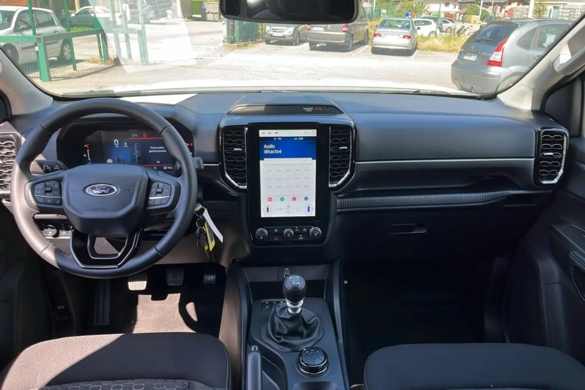 Vue intérieure avant du Ford Ranger 2025, tableau de bord noir avec écran tactile vertical et volant multifonctions.
