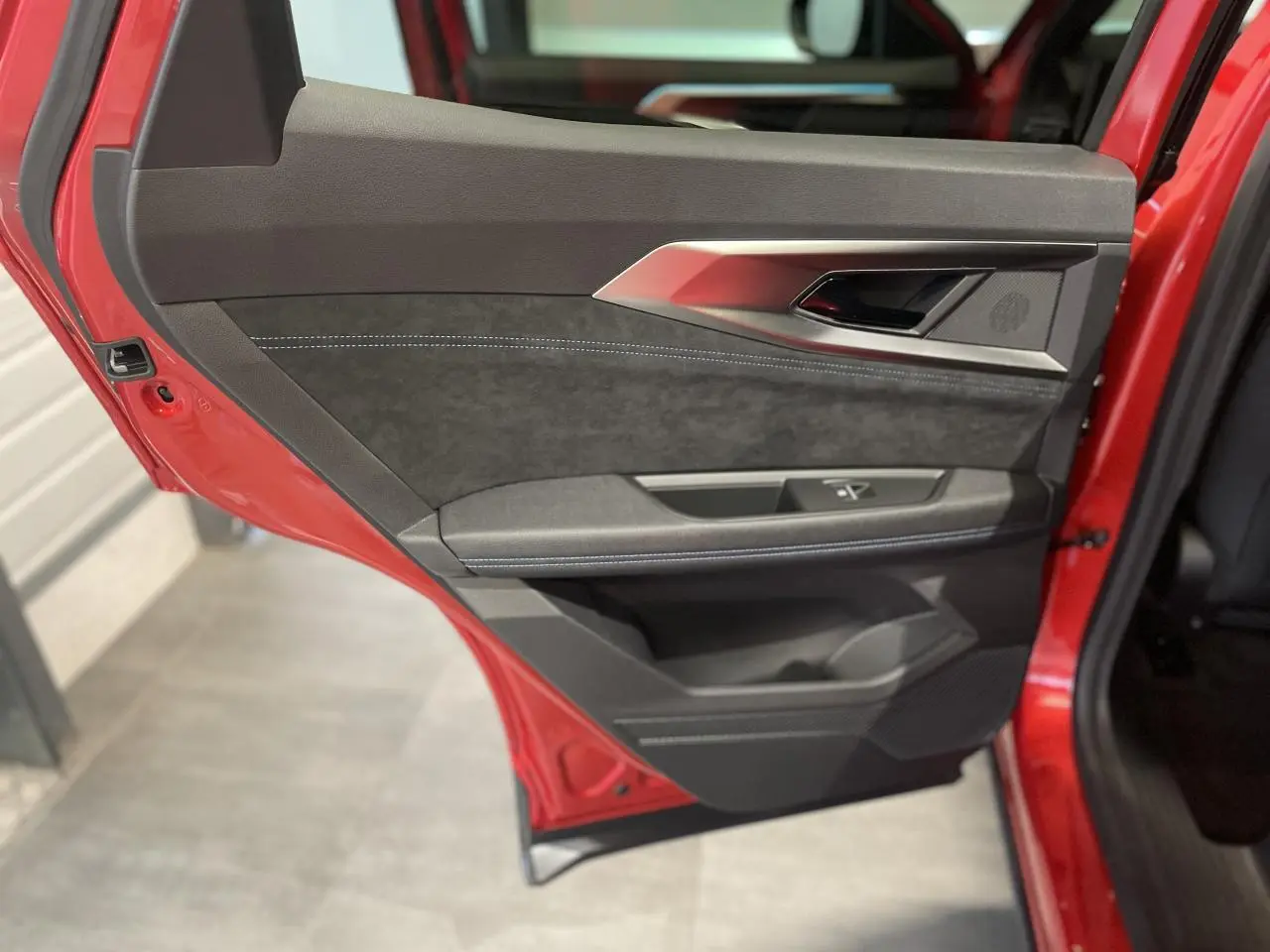 Vue rapprochée de la porte arrière gauche rouge métallisé du Renault Austral avec garniture noire et surpiqûres blanches.