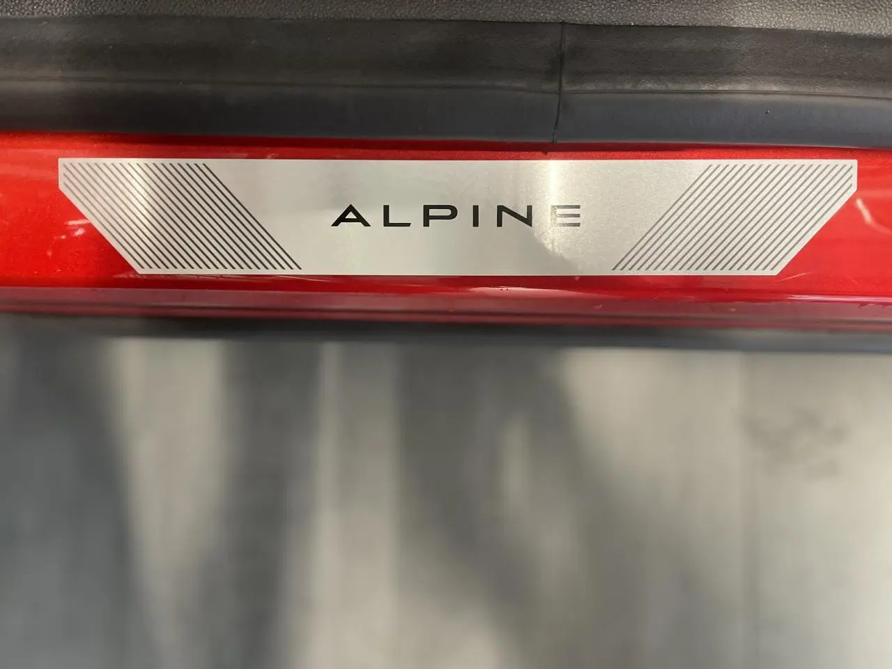 Gros plan sur la plaque de seuil de porte "ALPINE" sur la carrosserie rouge métallisée du Renault Austral.
