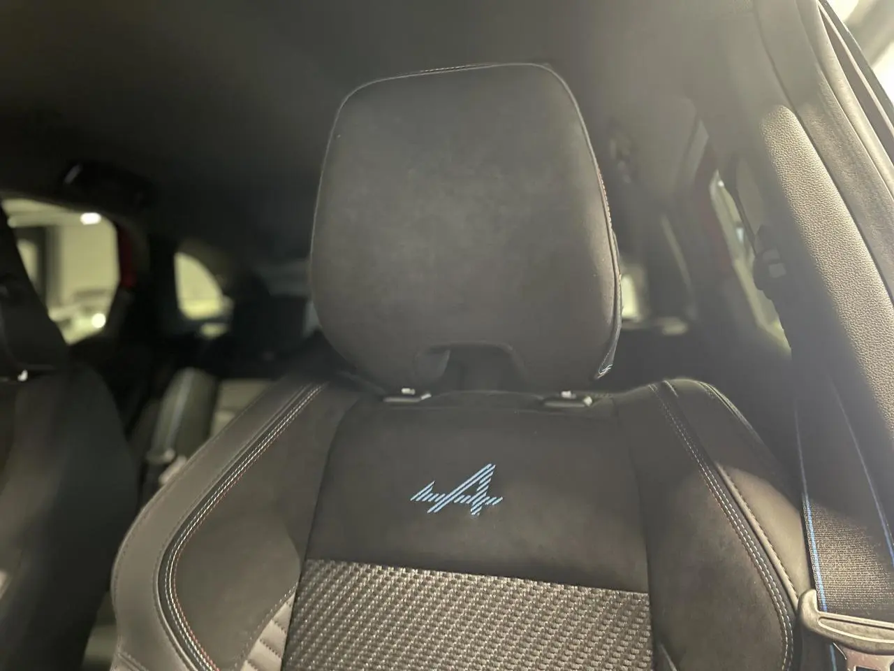 Gros plan sur le siège avant en Alcantara noir avec logo Alpine bleu et surpiqûres tricolores du Renault Austral.