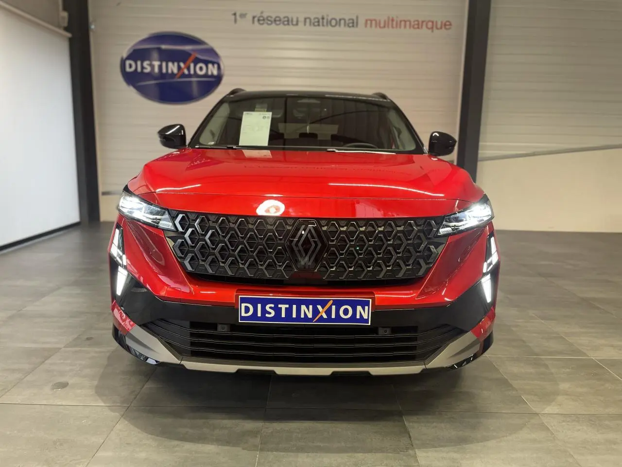 Vue frontale du Renault Austral rouge métallisé avec calandre noire et toit noir en showroom.