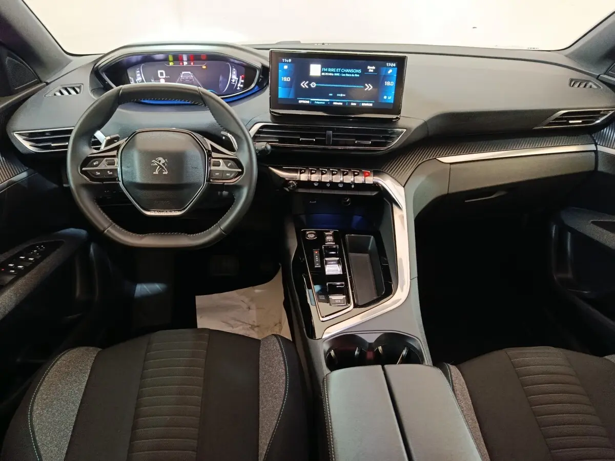 Vue intérieure avant du Peugeot 5008 2023, tableau de bord noir avec écran tactile central et volant cuir multifonctions.