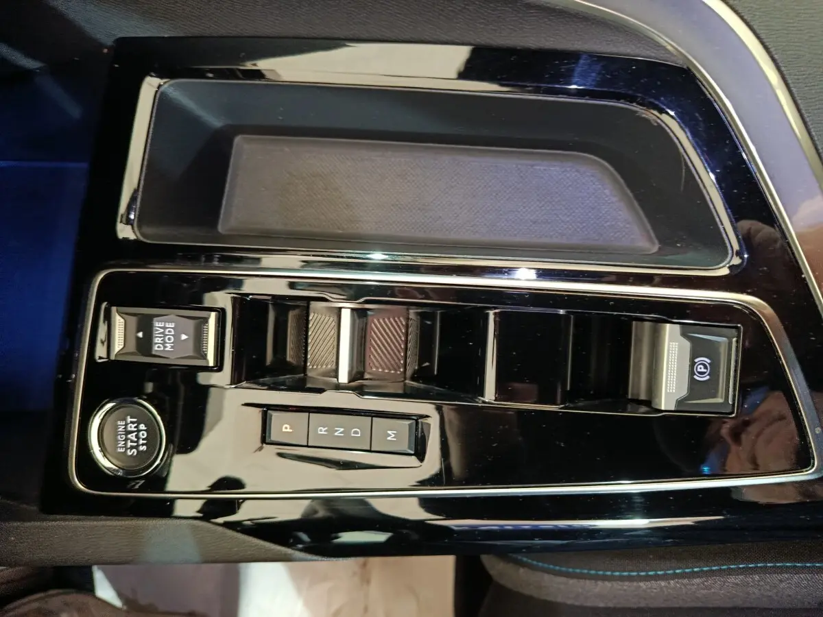 Gros plan sur la console centrale noire brillante du Peugeot 5008 2023 avec boutons de boîte auto et démarrage moteur.