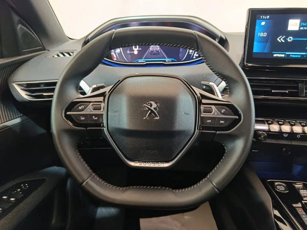 Vue rapprochée du volant cuir multifonctions noir du Peugeot 5008 2023 avec tableau de bord digital et écran tactile.