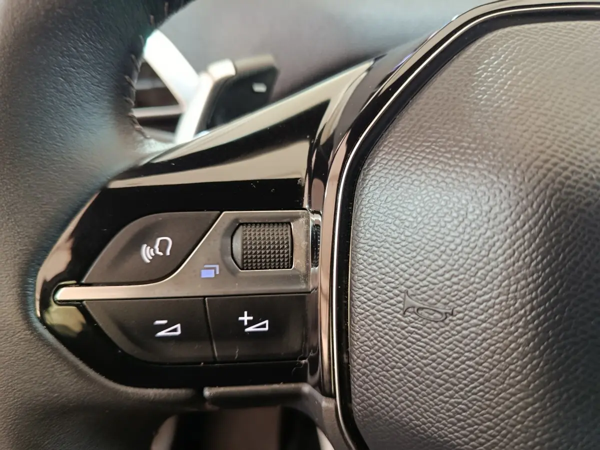 Gros plan sur les commandes multifonctions du volant cuir noir du Peugeot 5008 gris clair, version 2023.