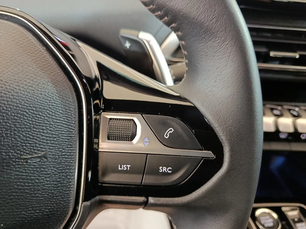 Gros plan sur le volant cuir noir multifonctions de la Peugeot 5008 2023, avec commandes audio et téléphone intégrées.