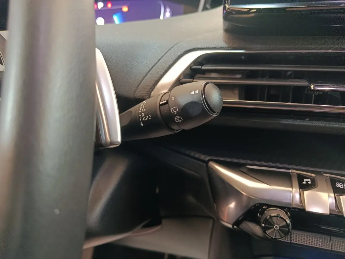 Gros plan sur la commande d’essuie-glace à gauche du volant cuir dans l’habitacle noir du Peugeot 5008 gris clair 2023.