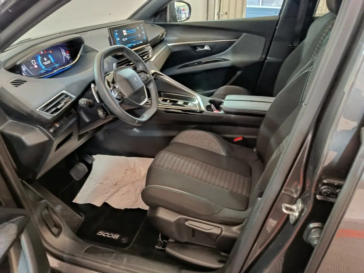 Vue intérieure côté conducteur du Peugeot 5008 gris clair 2023, avec volant cuir multifonctions et tableau de bord digital.