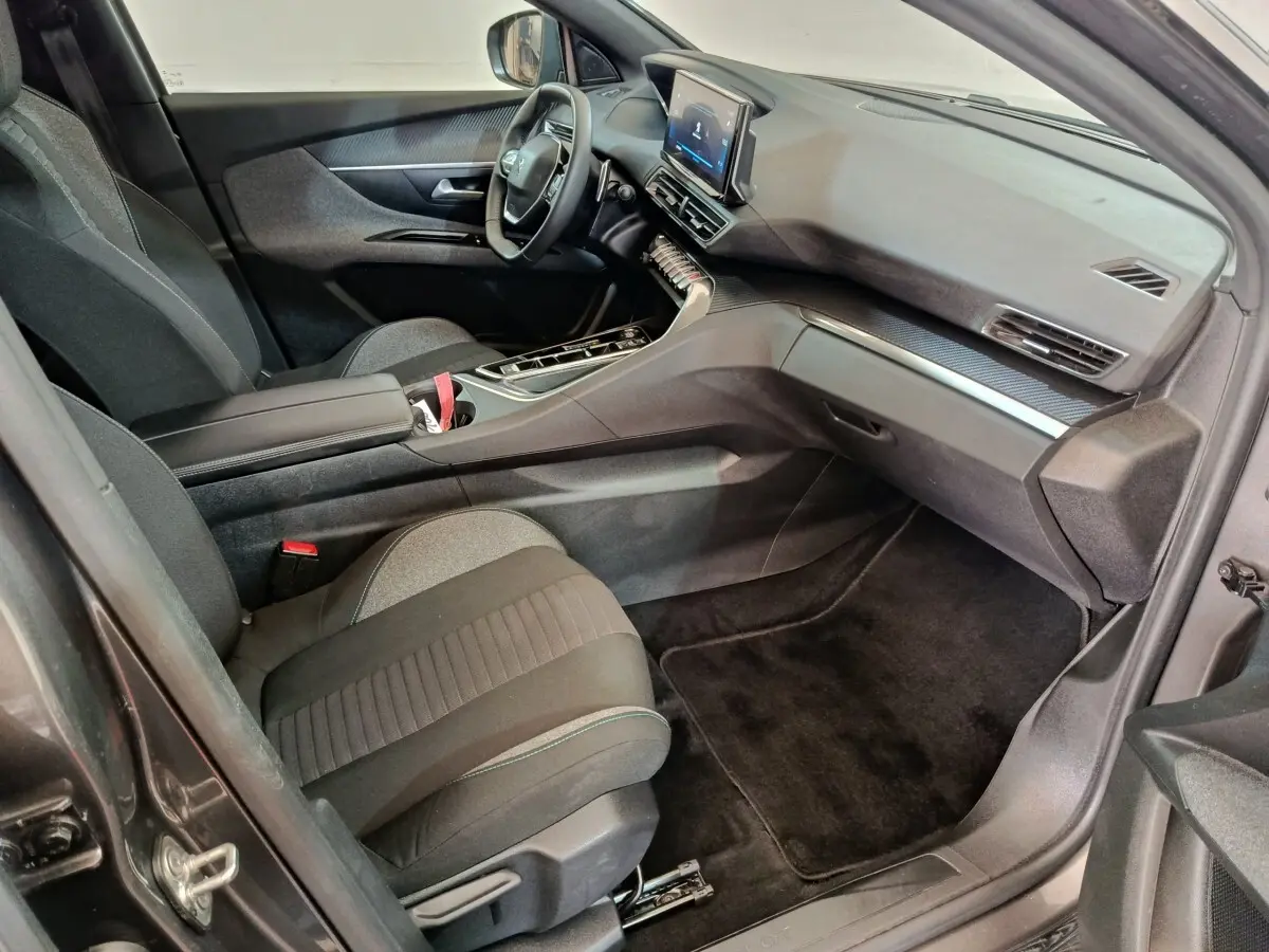 Vue intérieure côté passager du Peugeot 5008 gris clair 2023, mettant en valeur le tableau de bord et les sièges tissu noirs.