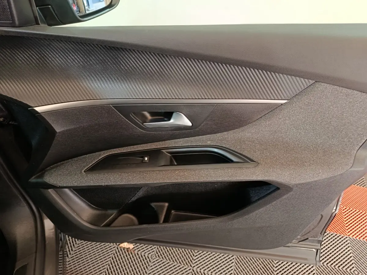 Gros plan sur la porte intérieure côté gauche du Peugeot 5008 gris clair, avec garniture textile et poignée argentée.