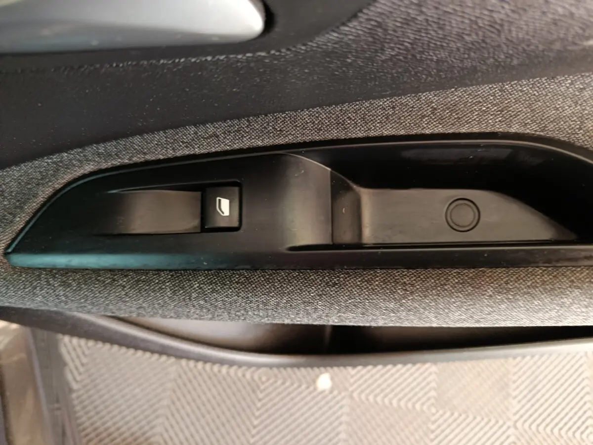 Gros plan sur la commande de lève-vitre noire intégrée à la garniture grise de la porte côté conducteur du Peugeot 5008 gris clair.