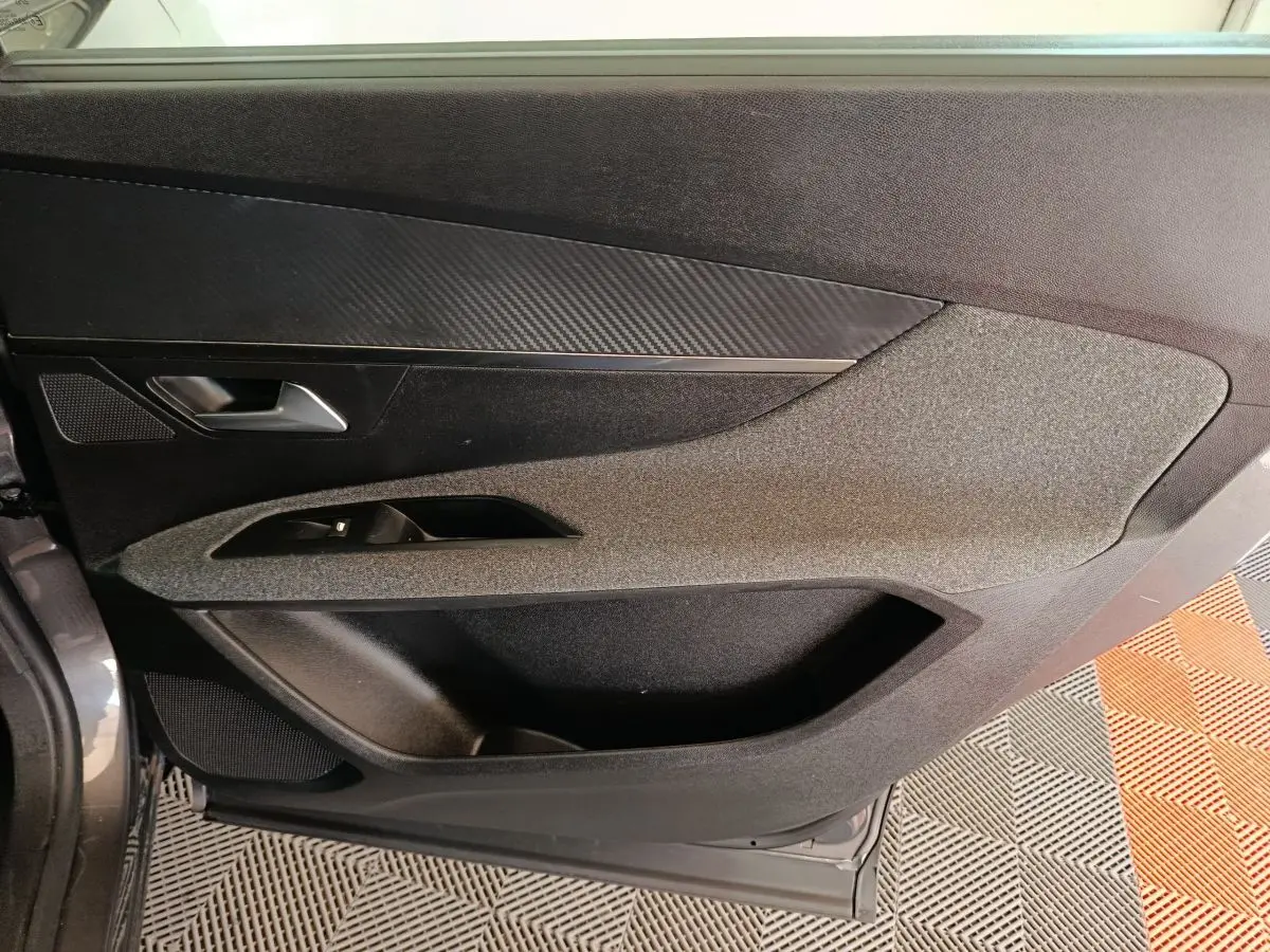Vue intérieure du panneau de porte avant gauche gris foncé du Peugeot 5008 2023 avec insert effet carbone et commande de vitre.