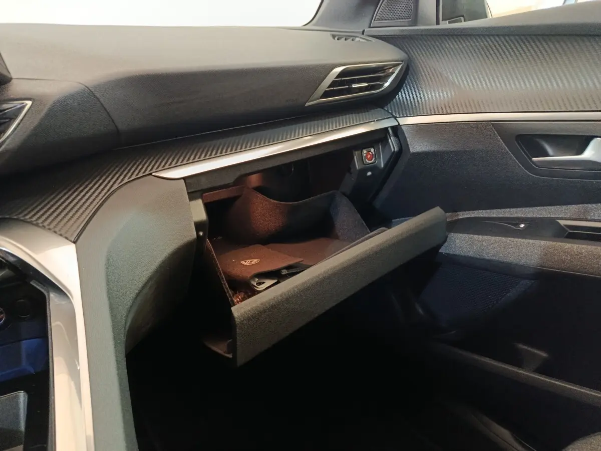 Intérieur côté passager du Peugeot 5008 gris clair 2023, avec boîte à gants ouverte et tableau de bord moderne.