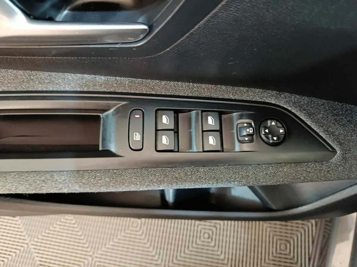 Gros plan sur les commandes de lève-vitres et rétroviseurs côté conducteur du Peugeot 5008 gris clair 2023.