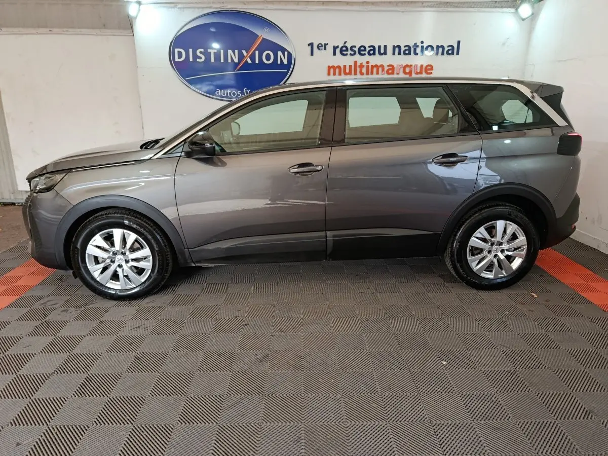 Vue de profil côté gauche d’un Peugeot 5008 gris clair de 2023, SUV familial avec jantes alliage et toit noir.