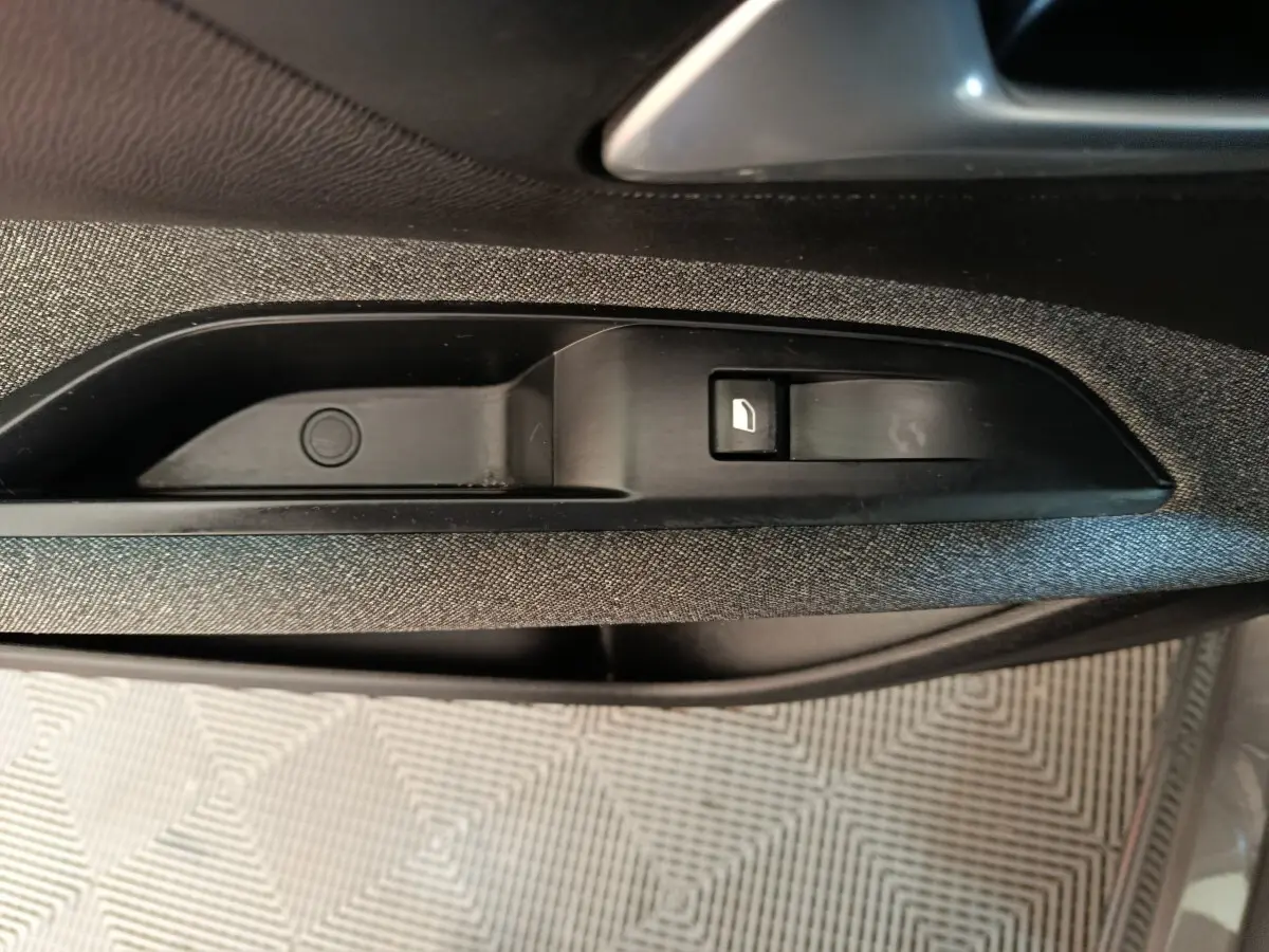 Détail de la commande de lève-vitre électrique sur la porte intérieure côté gauche du Peugeot 5008 gris clair 2023.