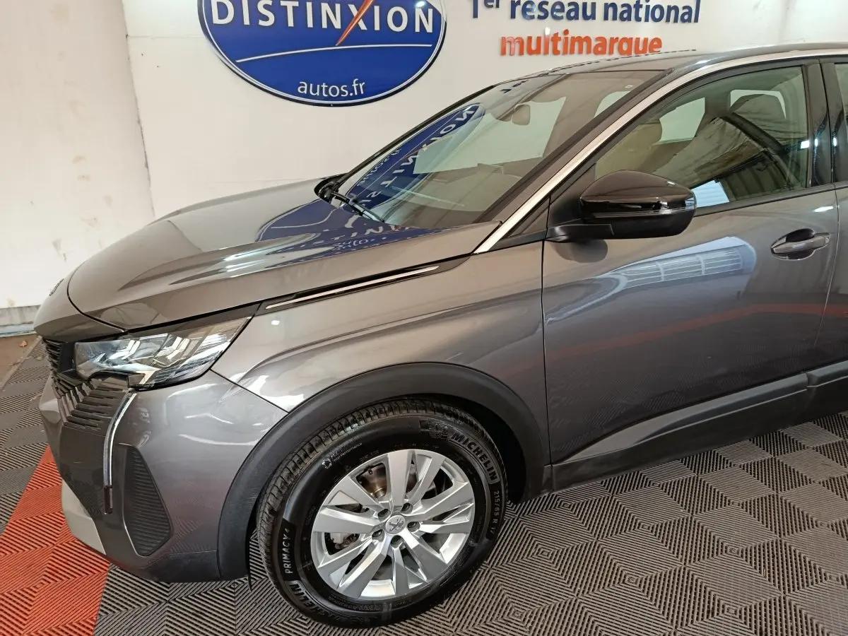 Vue 3/4 avant droit d’un Peugeot 5008 gris clair 2023 avec jantes alliage et rétroviseur noir brillant.