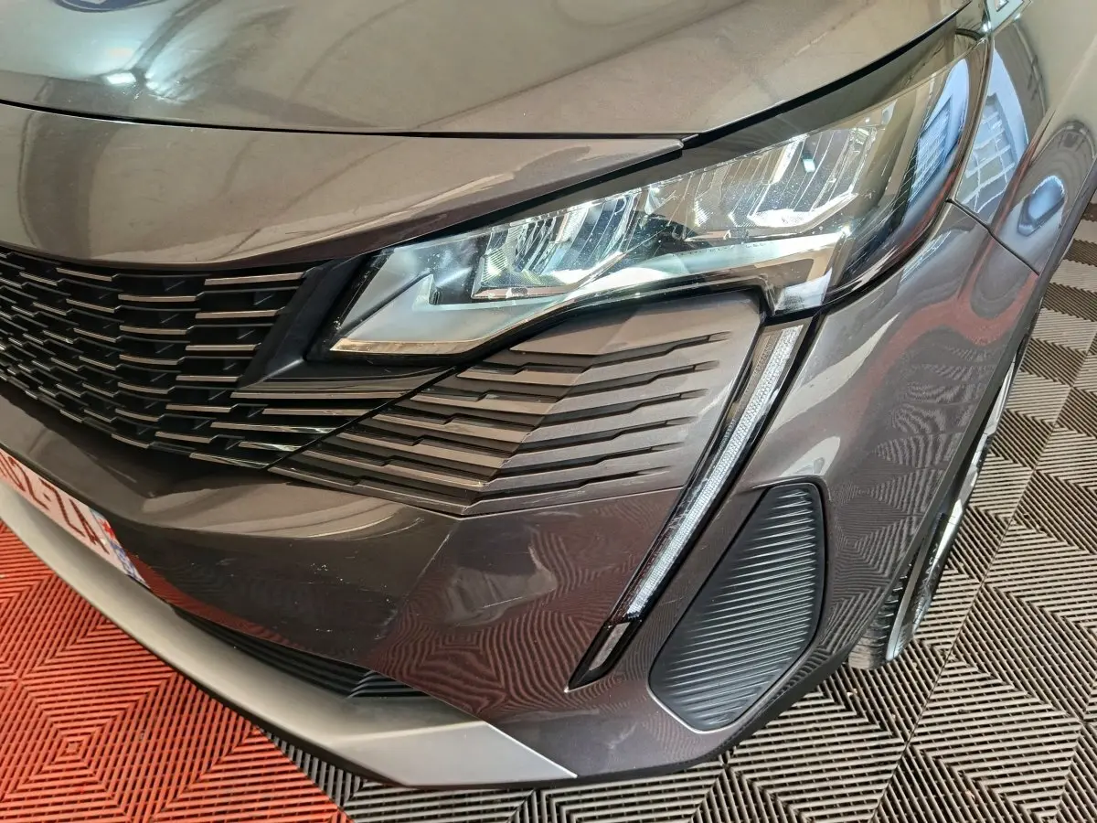 Gros plan sur l’avant droit gris clair du Peugeot 5008 2023, mettant en valeur le phare LED et la calandre distinctive.