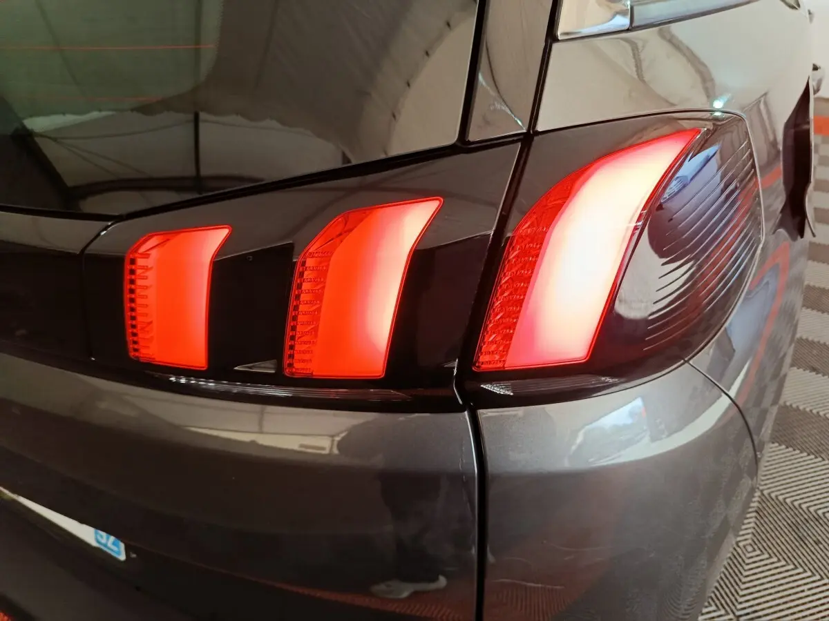 Gros plan sur le feu arrière droit rouge d’un Peugeot 5008 gris clair, avec reflet du plafond sur la carrosserie.
