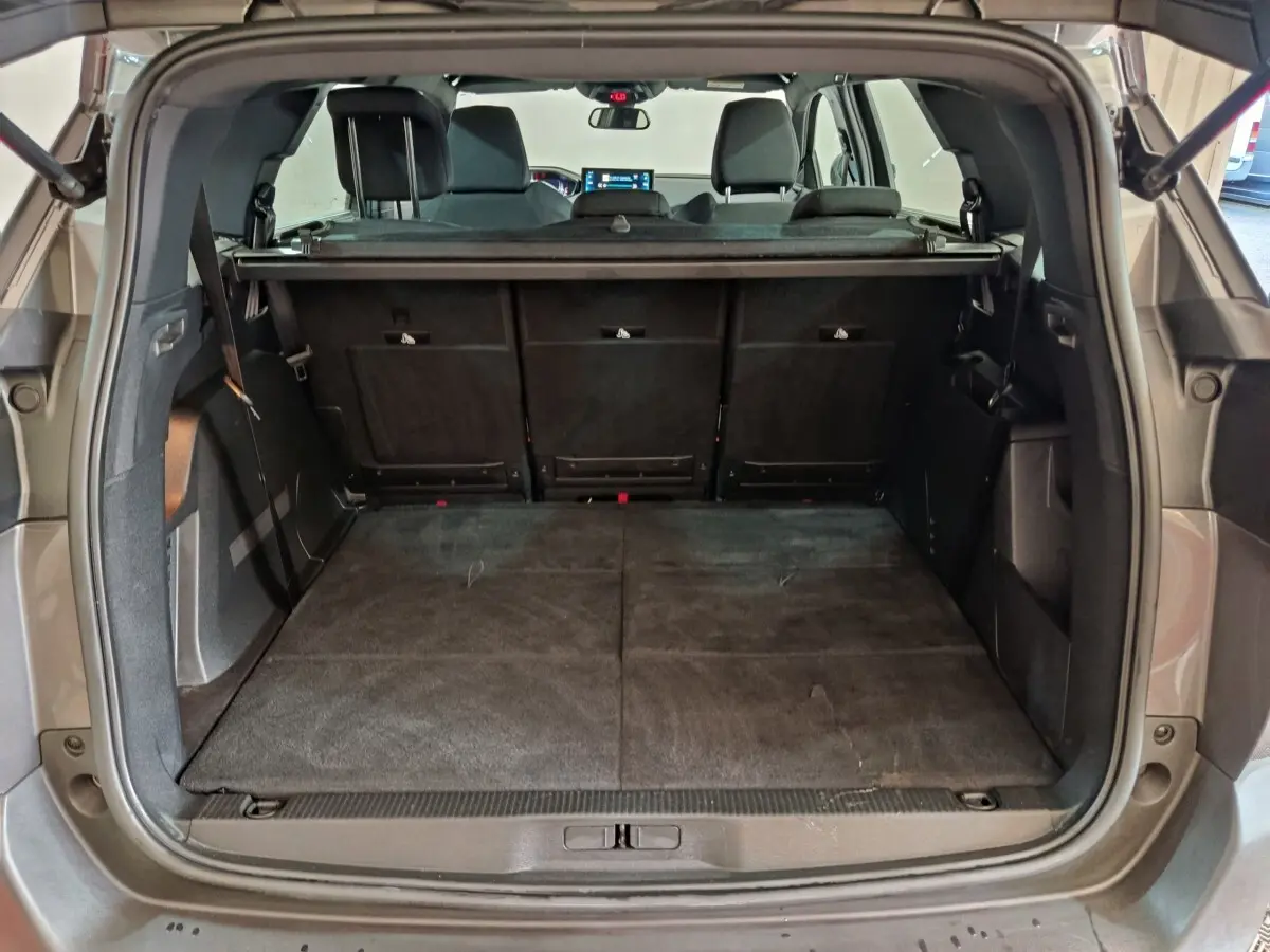 Vue arrière du coffre ouvert d'un Peugeot 5008 gris clair 2023 avec banquette arrière rabattue et tablette de coffre visible.