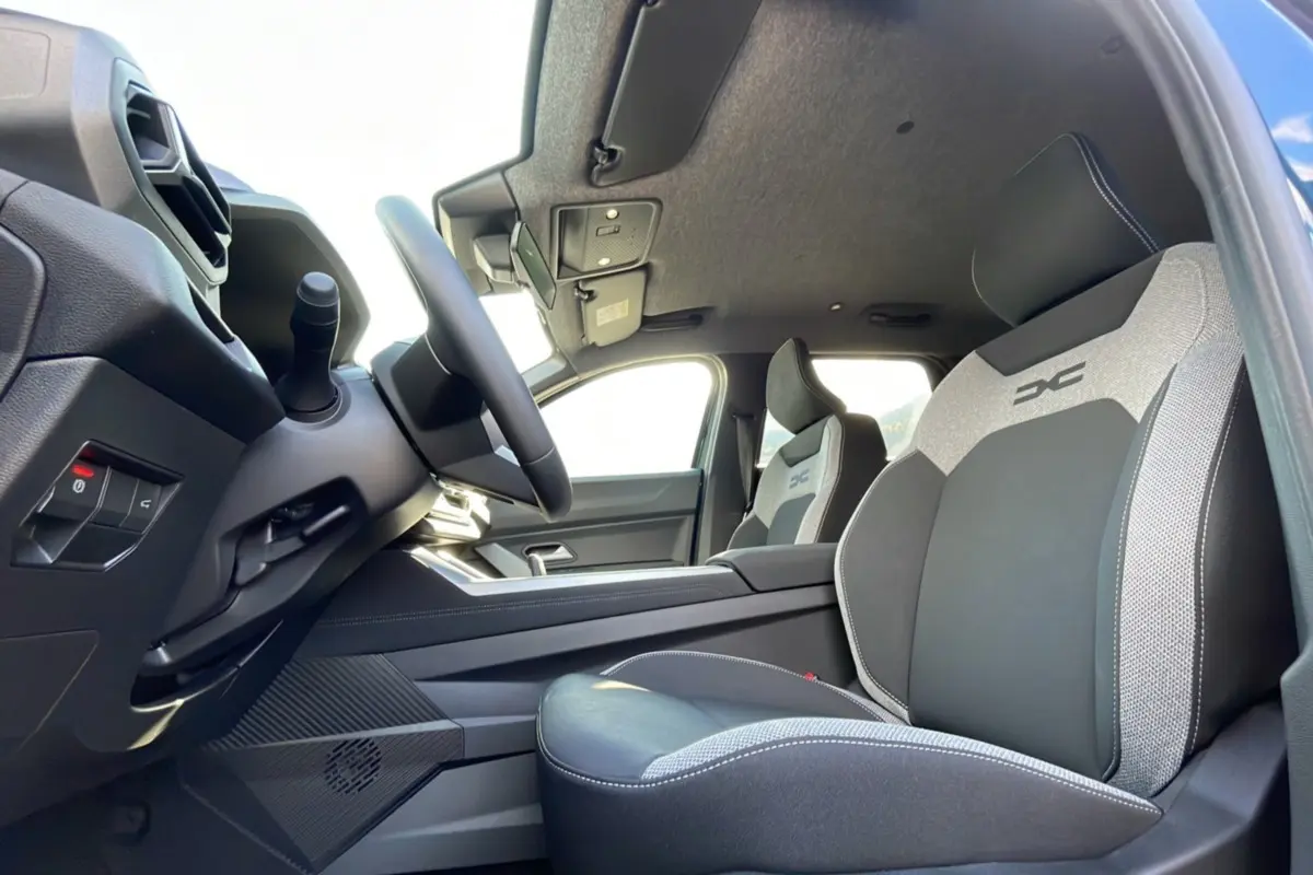 Intérieur du Dacia Bigster Hybrid 155 Journey City, vue côté conducteur, sièges bi-matière gris et noir avec logo DC.