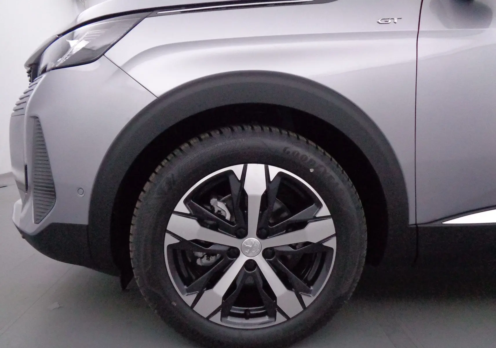 Gros plan sur la roue avant gauche du Peugeot 3008 gris Artense Métal avec jante alliage bicolore et badge GT visible.