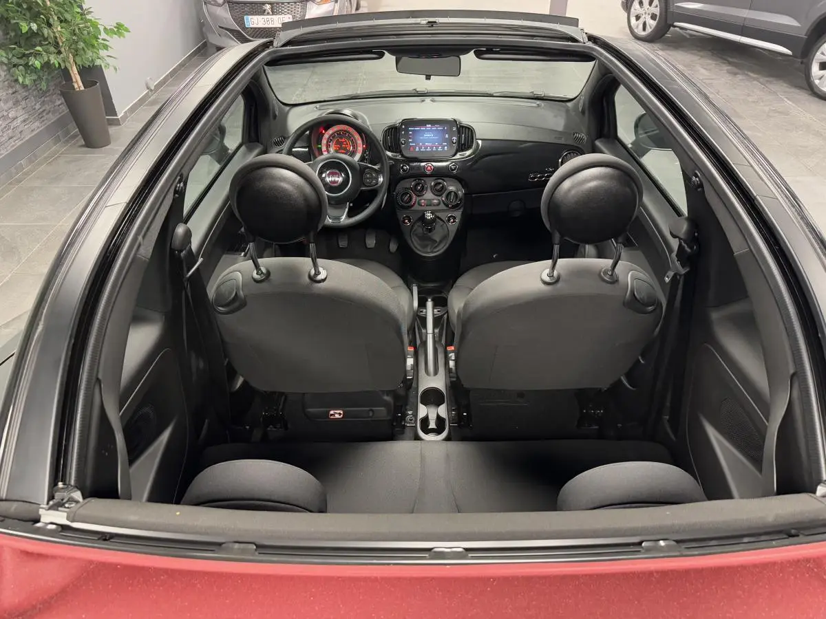 Vue intérieure arrière du cabriolet Fiat 500 noir avec capote rouge, volant noir et tableau de bord moderne.