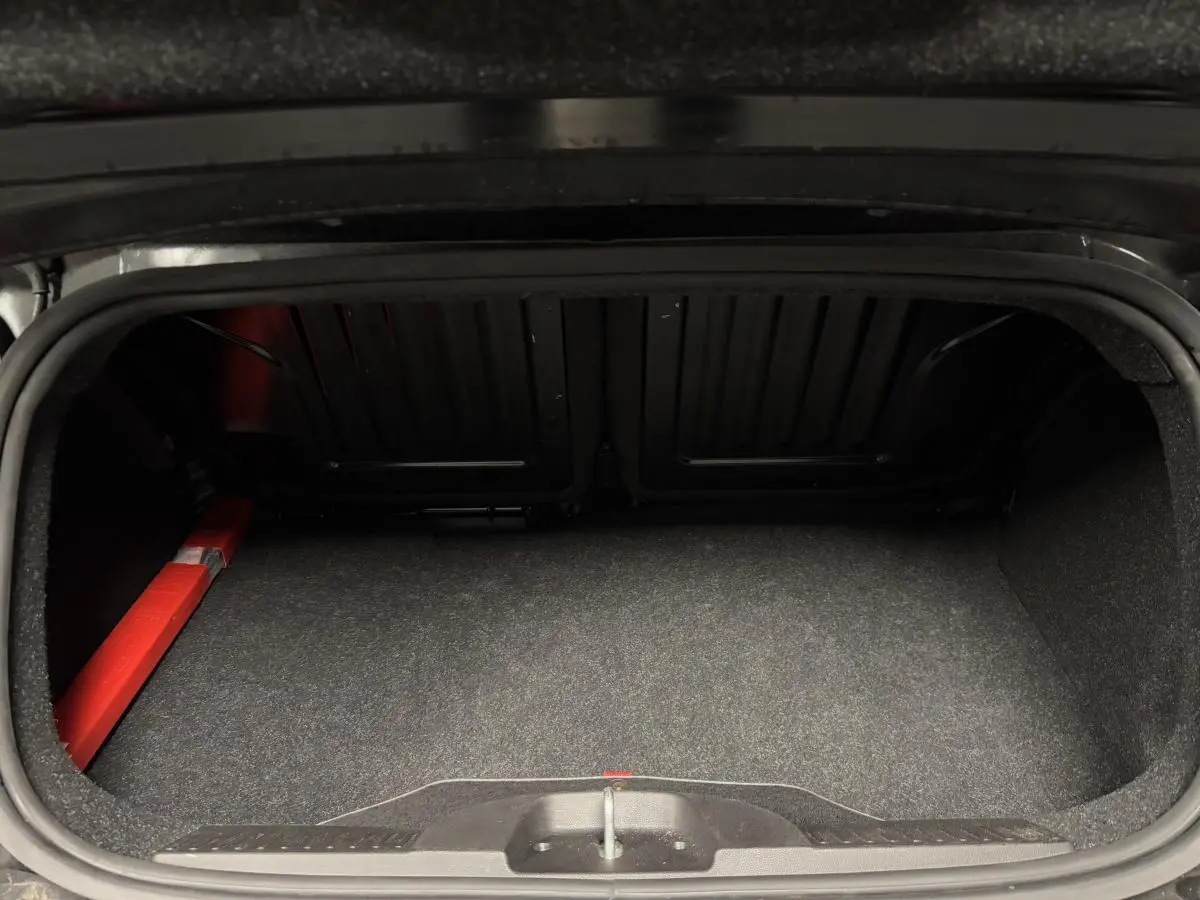 Coffre ouvert de la Fiat 500 Cabriolet noire, montrant l'espace de rangement et la capote rouge repliée.