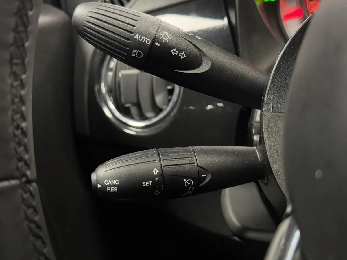 Gros plan sur les commandes au volant noir de la Fiat 500 Cabriolet 2024 avec détails des fonctions d'éclairage et régulateur de vitesse.