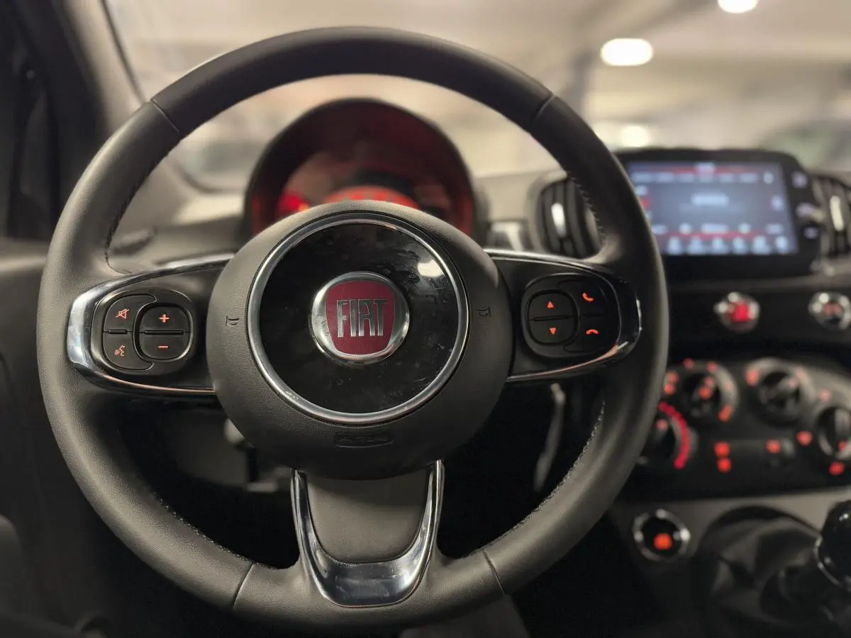 Volant noir en éco-cuir de la Fiat 500 Cabriolet 2024 avec commandes intégrées et tableau de bord flou en arrière-plan