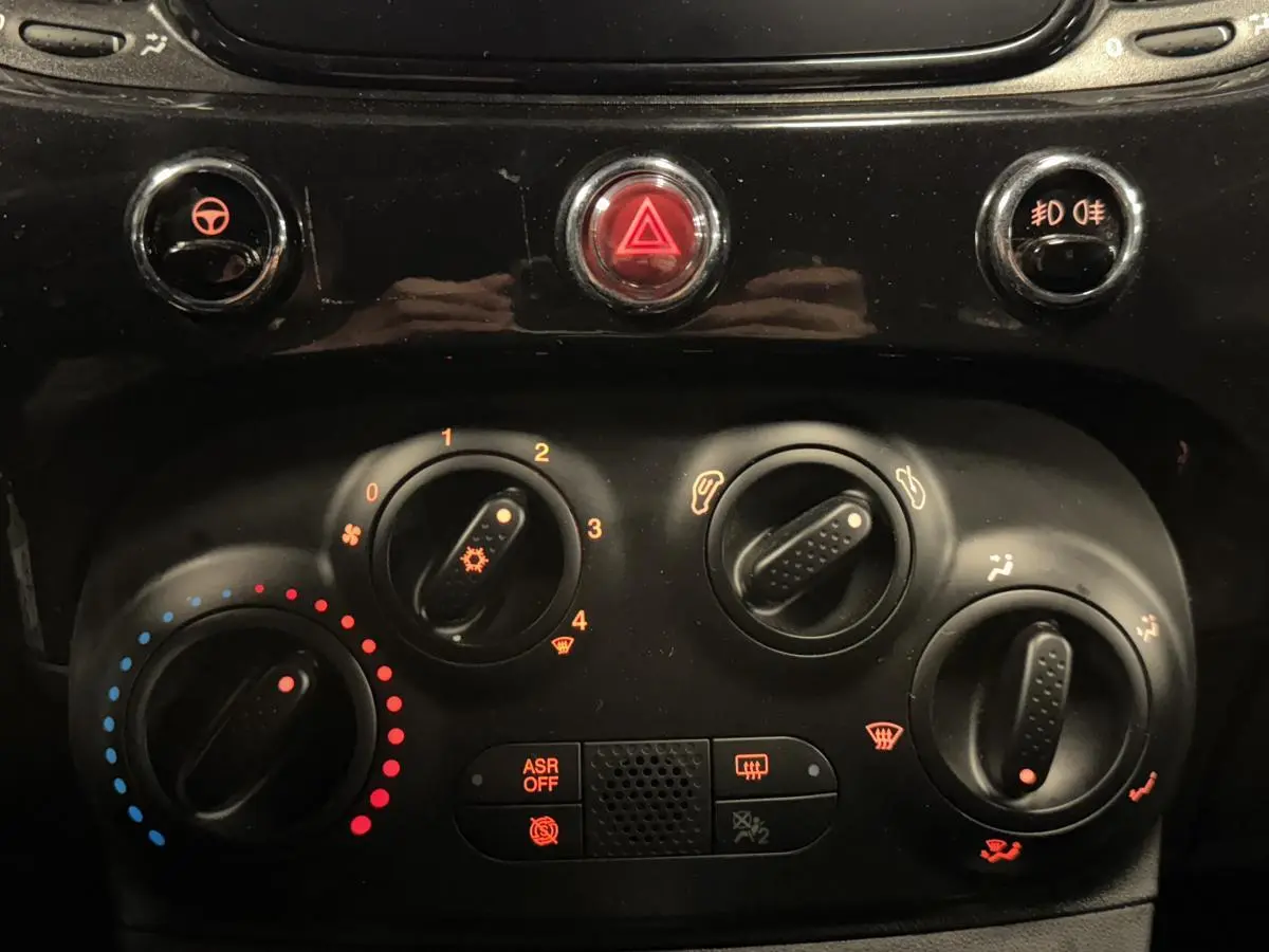 Gros plan sur la console centrale noire de la Fiat 500 Cabriolet 2024 avec commandes de climatisation manuelle et boutons lumineux.