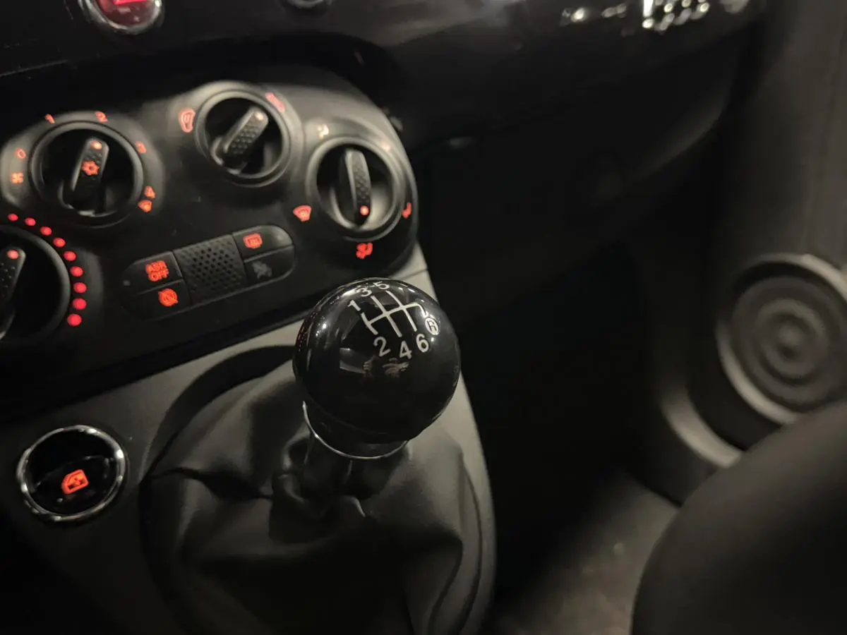 Gros plan sur le levier de vitesses manuel noir et les commandes de climatisation du tableau de bord d'une Fiat 500 Cabriolet noire.