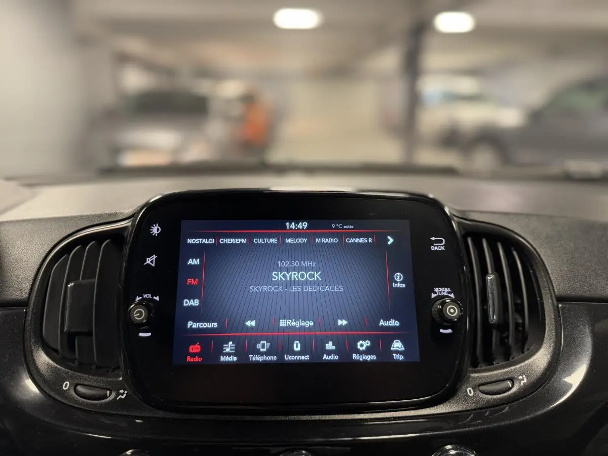 Gros plan sur l'écran tactile central de la Fiat 500 Cabriolet noire, affichant la radio Skyrock en intérieur voiture.