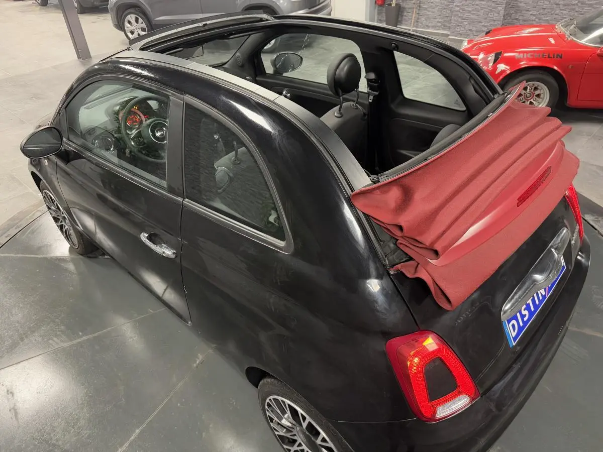 Vue 3/4 arrière droite d'une Fiat 500 Cabriolet noire avec capote rouge partiellement repliée et jantes alliage 16 pouces.