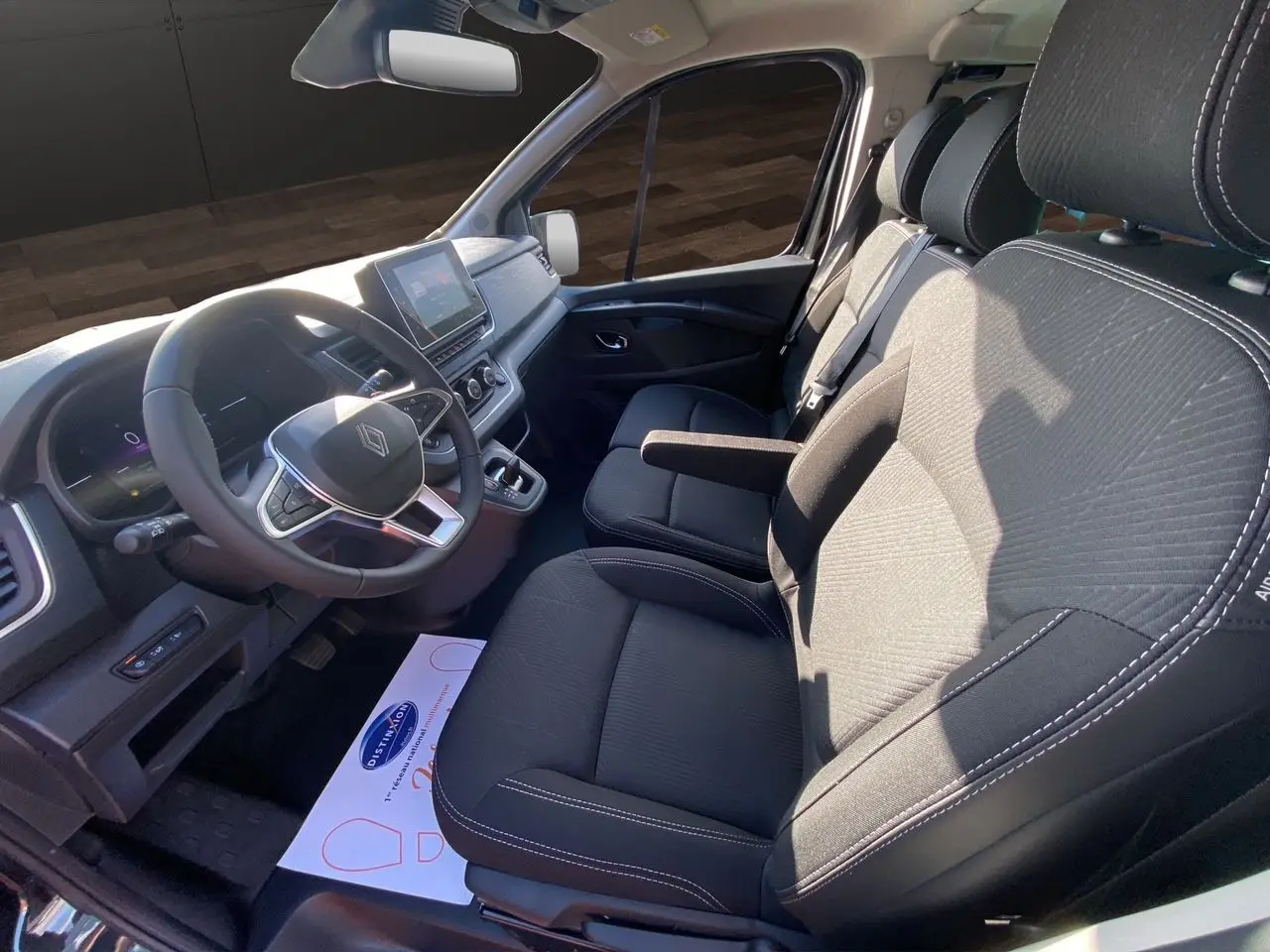 Intérieur avant du Renault Trafic Combi noir 2025, sièges tissu noir et tableau de bord avec écran tactile central.