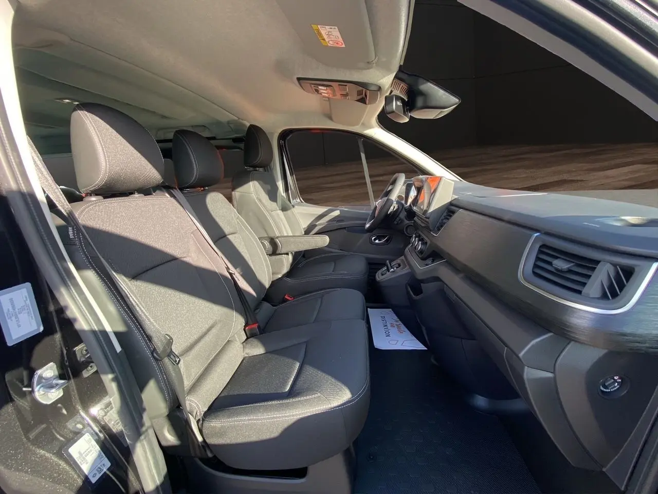 Intérieur avant du Renault Trafic Combi noir 2025, sièges tissu noir avec accoudoirs et tableau de bord moderne.