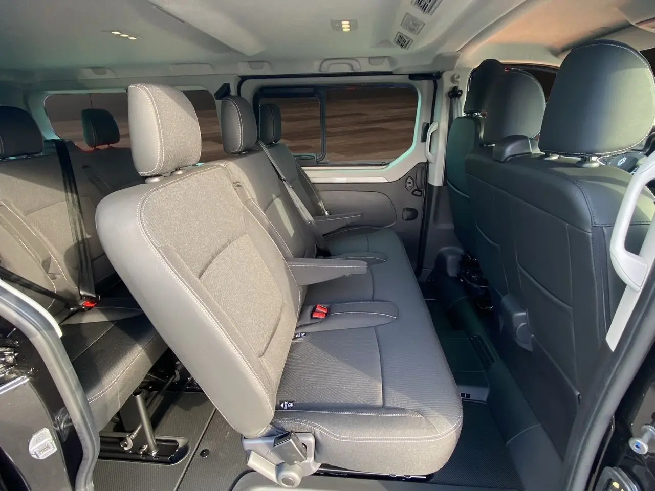 Intérieur du Renault Trafic Combi 2025 vu côté gauche, banquettes tissu noir avec accoudoirs et ceintures de sécurité.