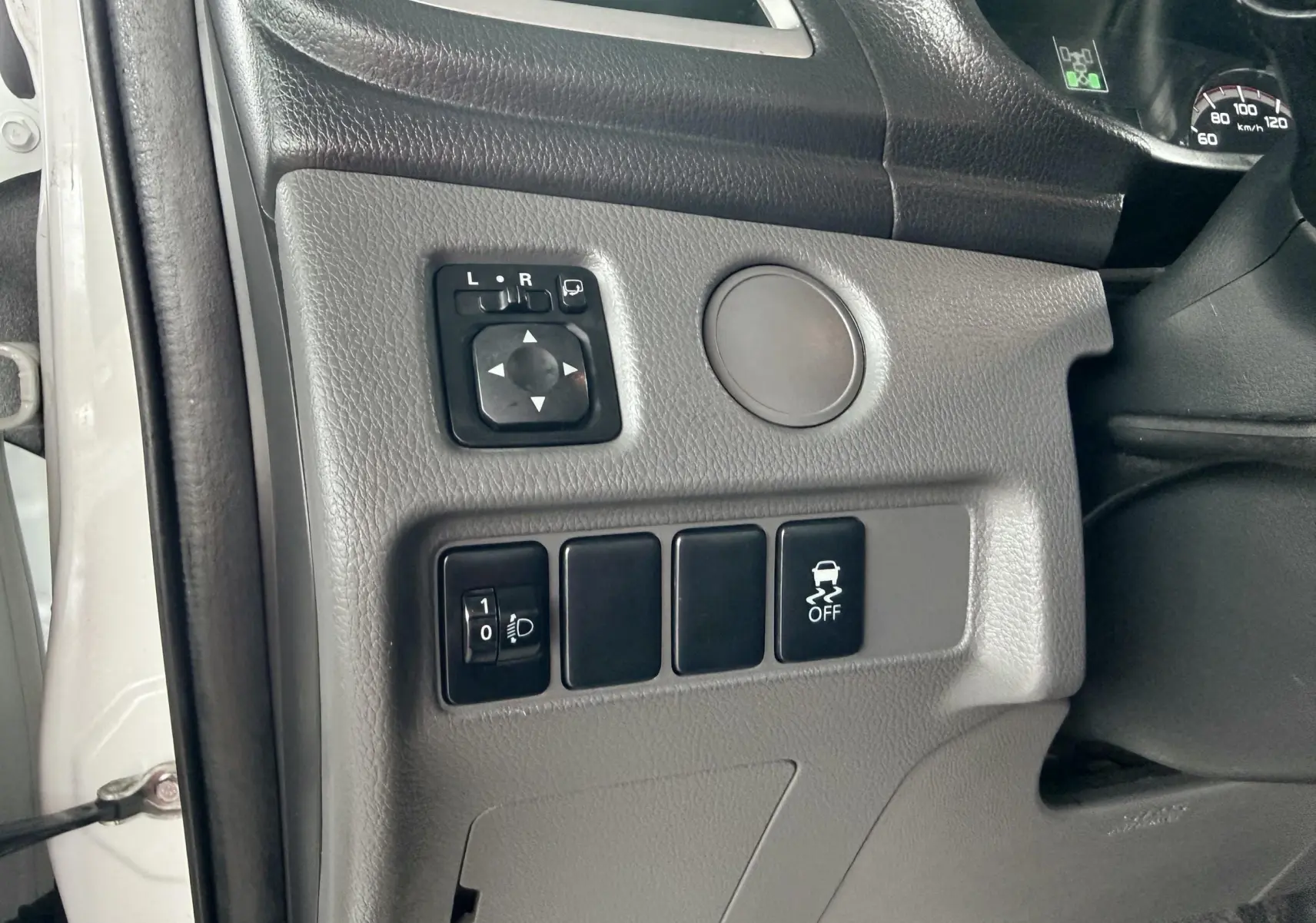 Vue rapprochée des commandes côté gauche du tableau de bord gris d’un Mitsubishi L200 blanc, avec réglage des rétroviseurs et bouton ESP.