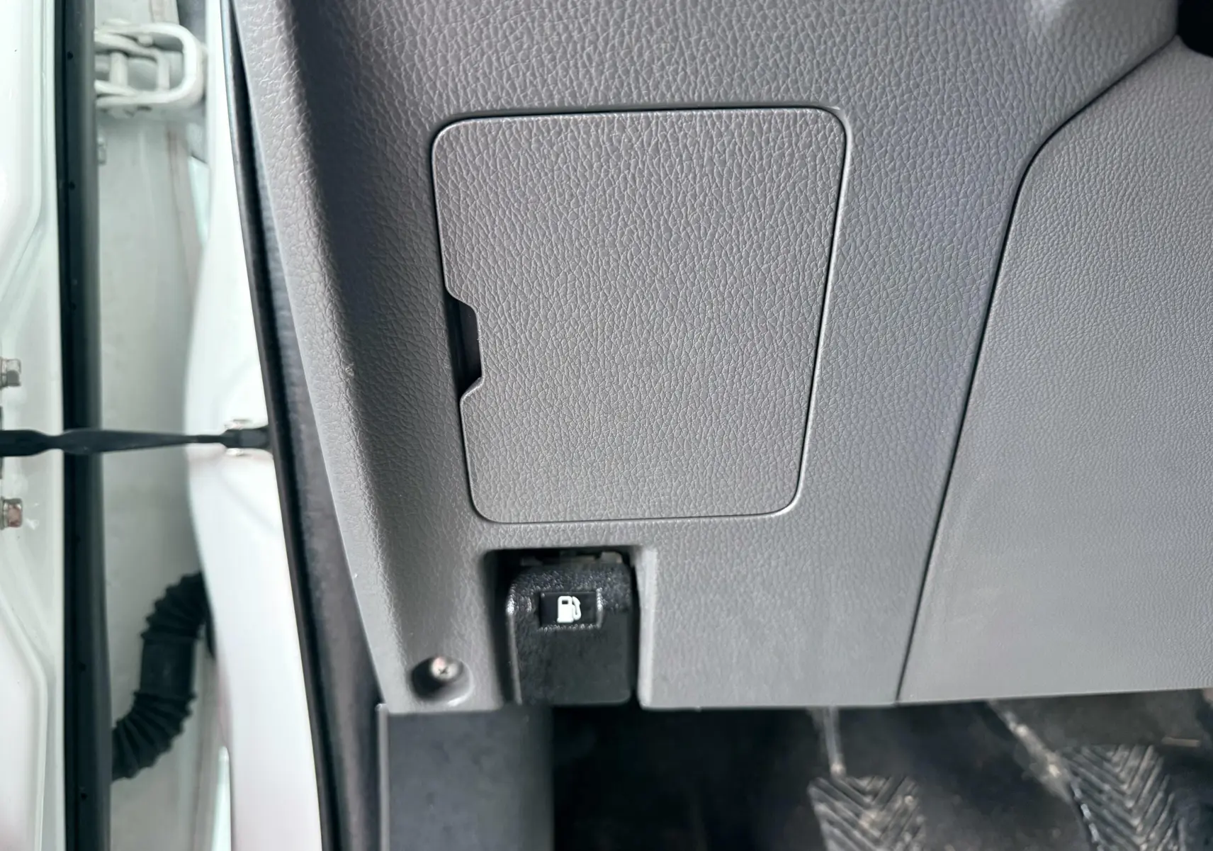 Détail intérieur montrant le levier d'ouverture de trappe à carburant sur la partie basse gauche du tableau de bord gris.