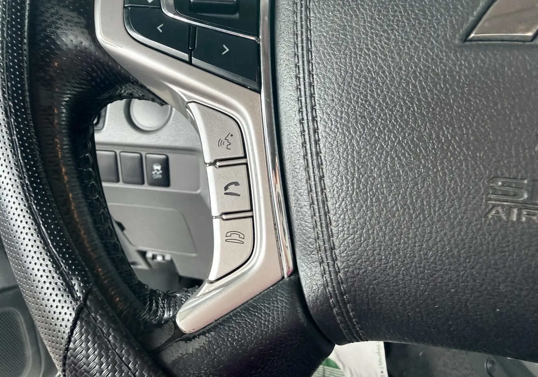 Gros plan sur le volant en cuir noir du Mitsubishi L200 blanc, montrant les commandes intégrées côté gauche.