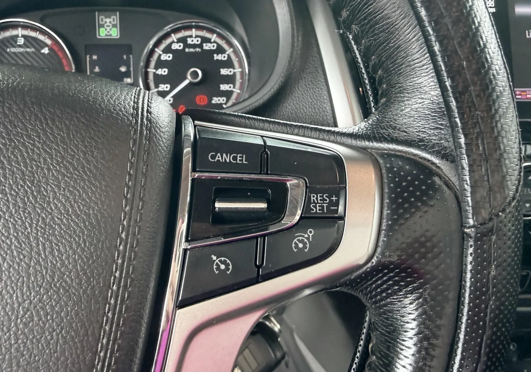 Gros plan sur les commandes de régulateur de vitesse au volant cuir du Mitsubishi L200 blanc, tableau de bord en arrière-plan.