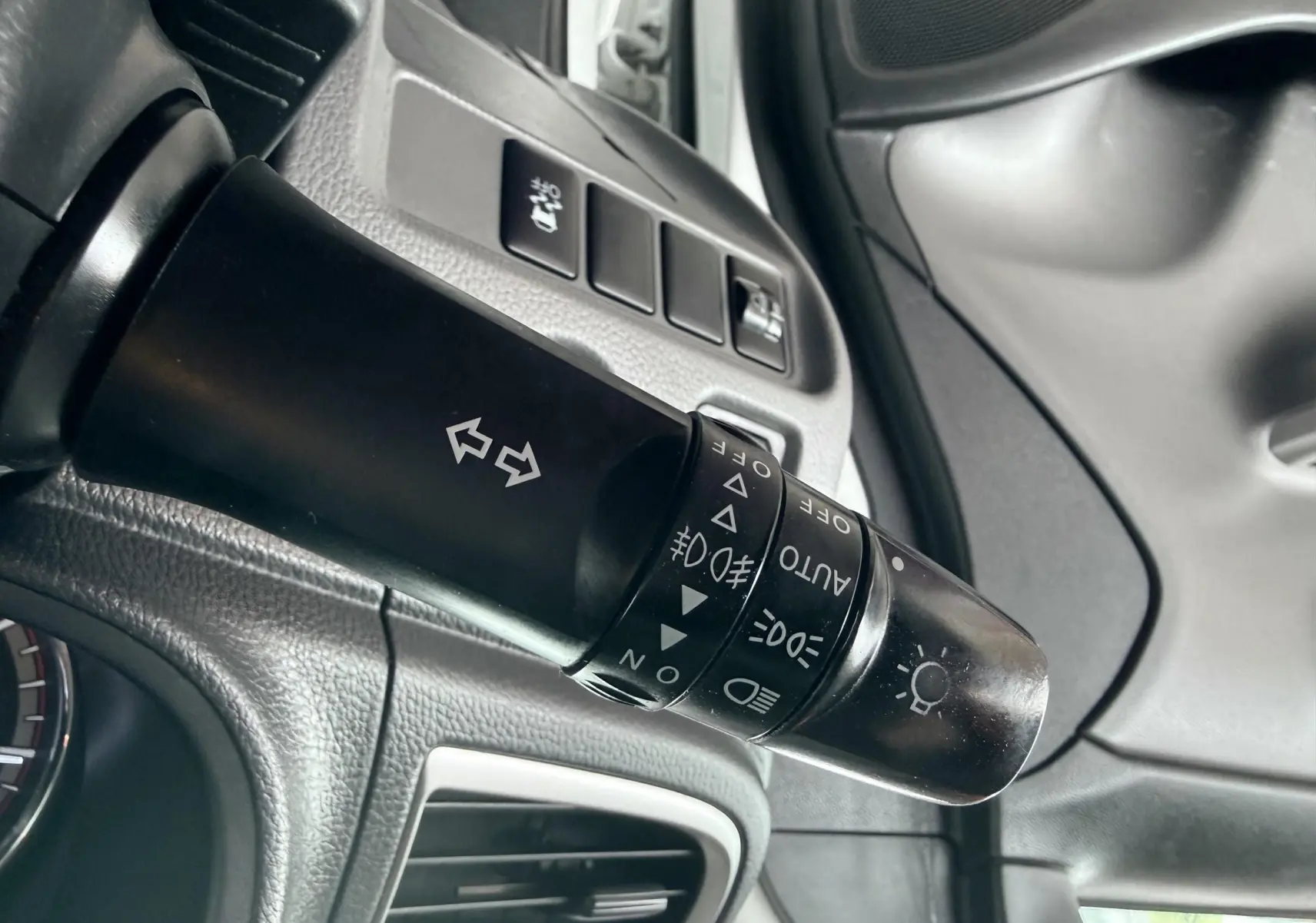 Gros plan sur la commande des phares et clignotants à gauche du volant dans l’habitacle gris du Mitsubishi L200 blanc.