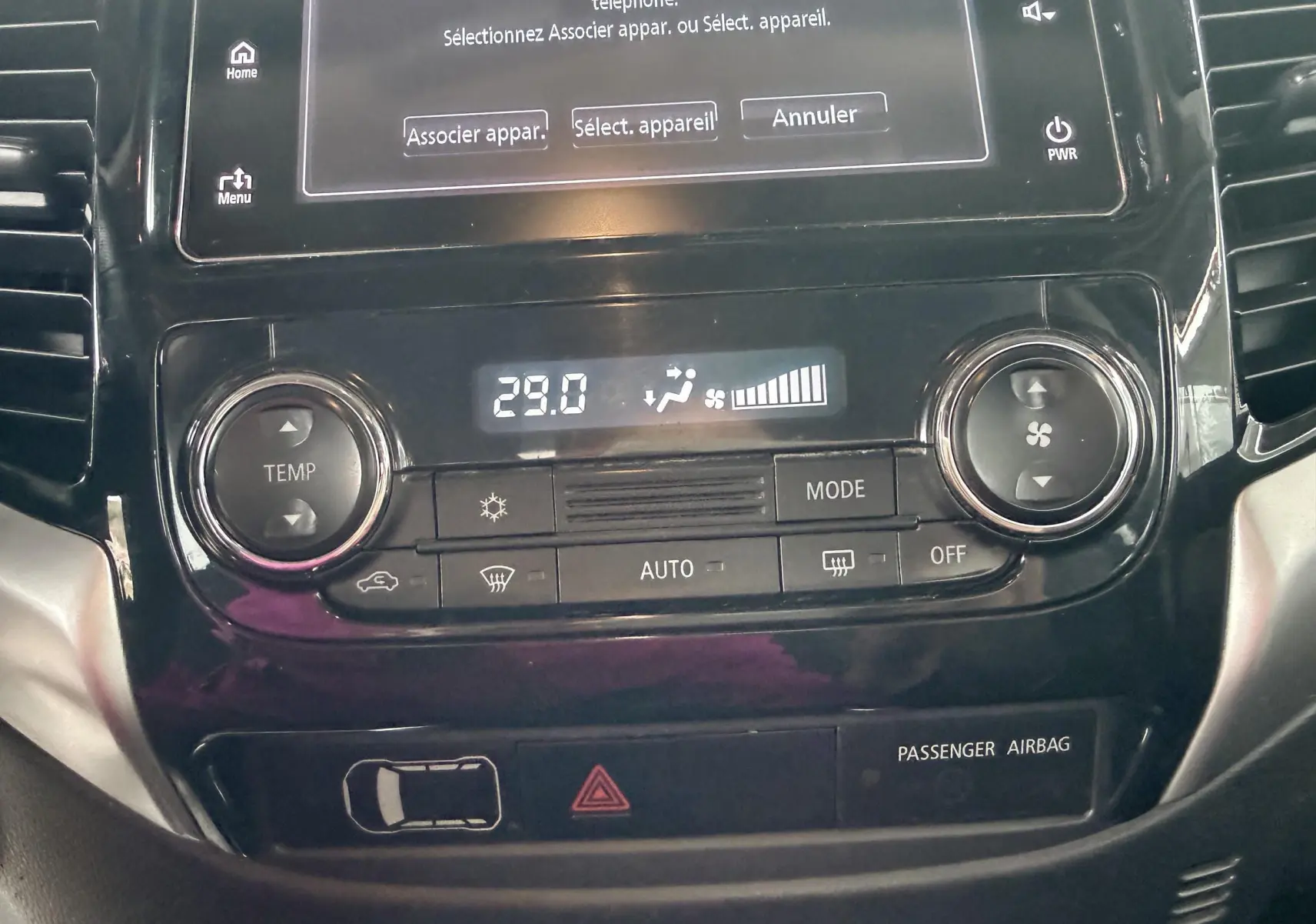 Gros plan sur la console centrale noire du Mitsubishi L200 blanc, affichant la climatisation à 29°C et les commandes tactiles.