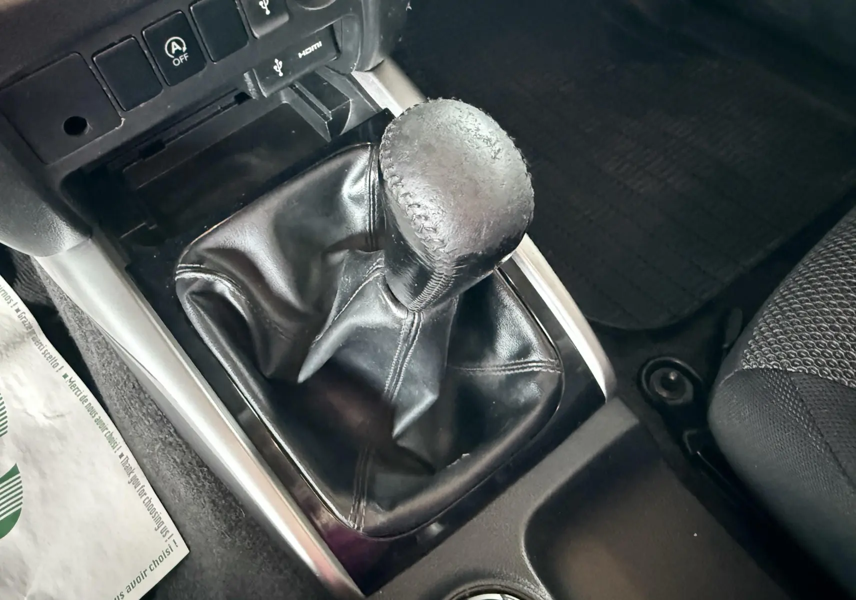 Gros plan sur le levier de vitesse manuel noir dans l’habitacle du Mitsubishi L200 blanc, avec console et sièges partiellement visibles.